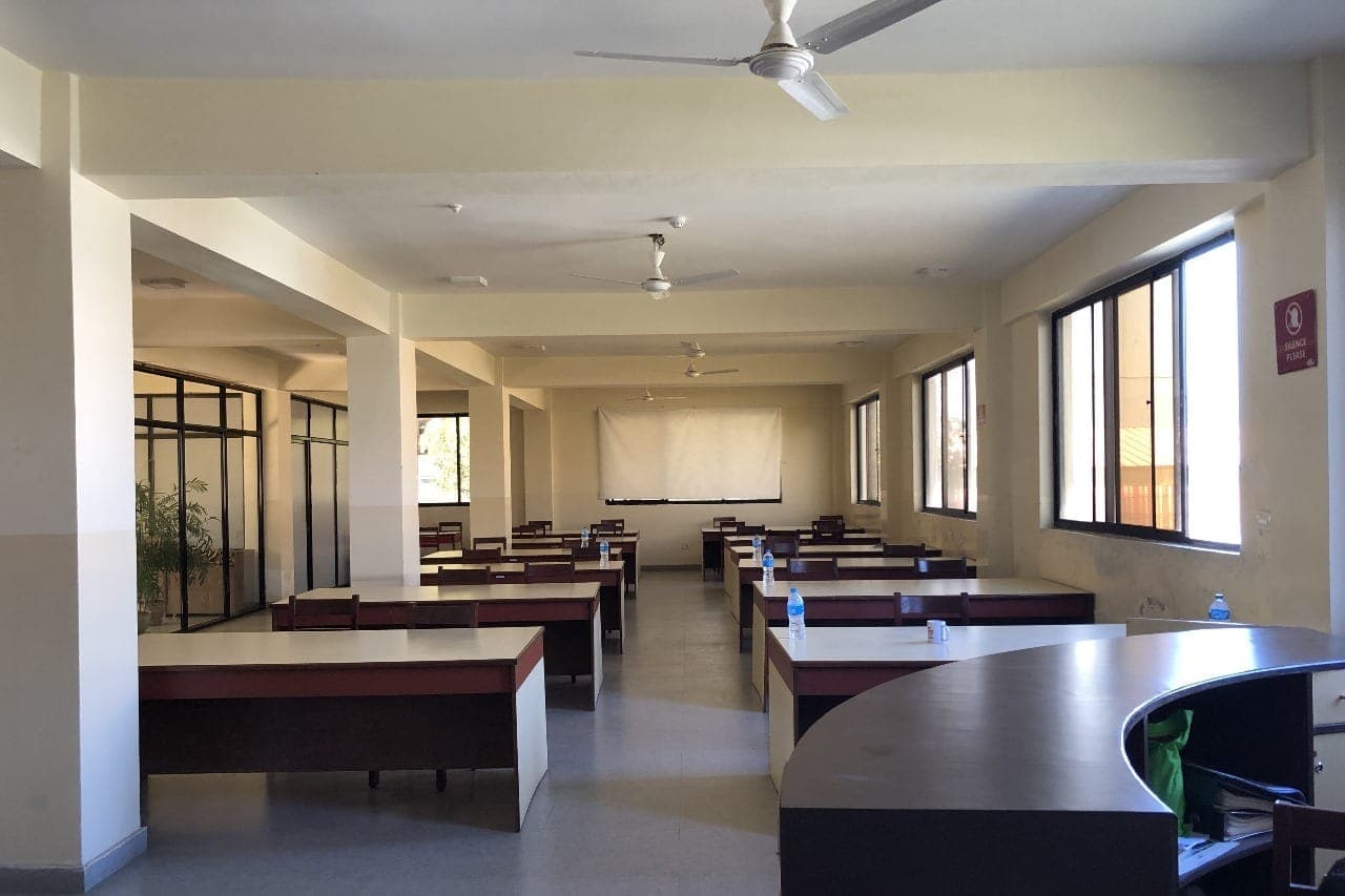 A NAMI reading hall, long study desks ranked beneath ceiling fans with a projection screen at the far end and a silence notice on the wall.
